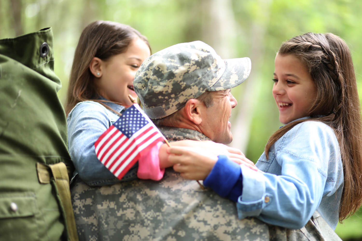 Family welcomes home a USA army soldier. The children excitedly hug father holding American flags.